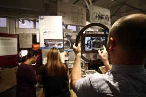 An augmented reality tablet in a car steering wheel shaped frame being used in the Lanchester Interactive Archive space at Coventry University library, 2017